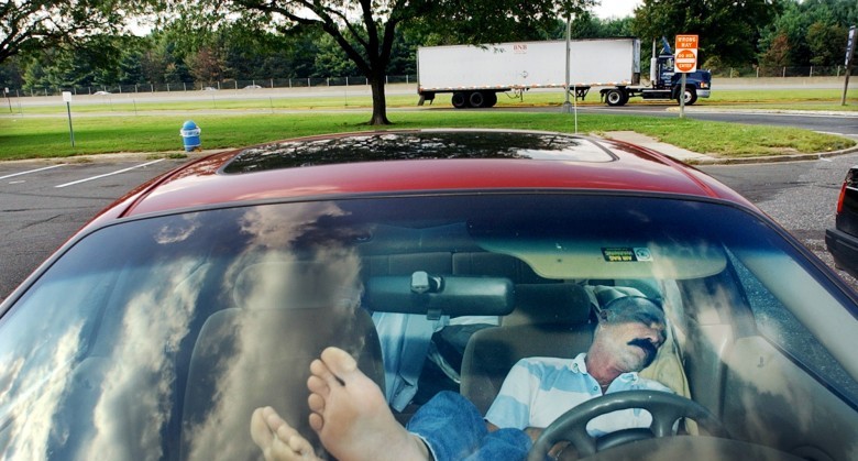 FILE - In this Sept. 25, 2003 file photo, an unidentified man rests his feet on the dashboard as he takes nap at a New Jersey Turnpike rest stop in Mount Laurel, N.J. The Centers for Disease Control and Prevention released its latest drowsy driving report on Thursday, July 3, 2014. According to a new survey, about 1 in 25 adults say they recently fell asleep while driving. (AP Photo/Daniel Hulshizer, File)