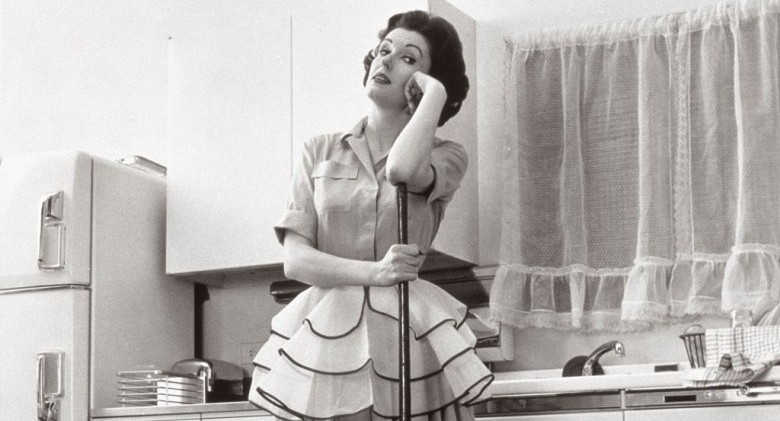 BR9E69 1950s WOMAN HOUSEWIFE STANDING IN KITCHEN LEANING ON BROOM