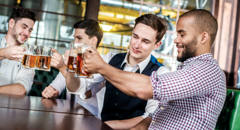 Four businessmen friends drink beer and spend time together in a bar. Confident business people having fun with friends at the bar with a beer at the table