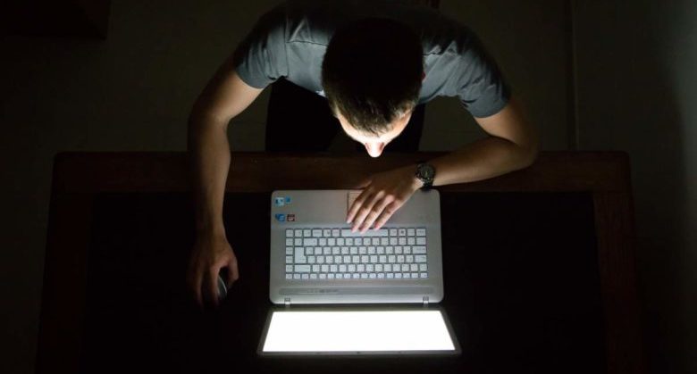 Guy checking internet with laptop at late night with dark room, view from above. Internet addiction.