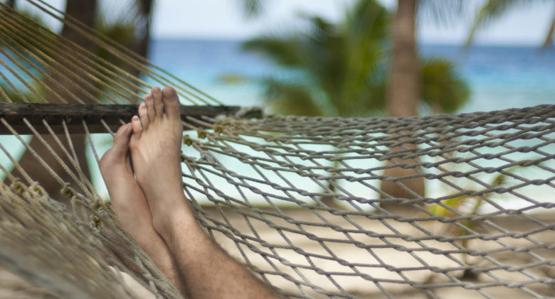 Cropped view of feet up in a hammock as a man takes a relaxing siesta in a tropical beachfront island resort