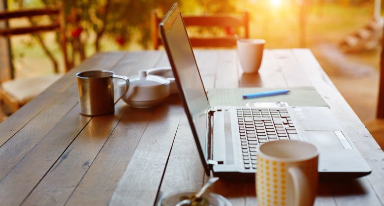 Laptop computer, phone and coffee in the garden - freelance or remote work concept. small depth of field, focus on the keyboard