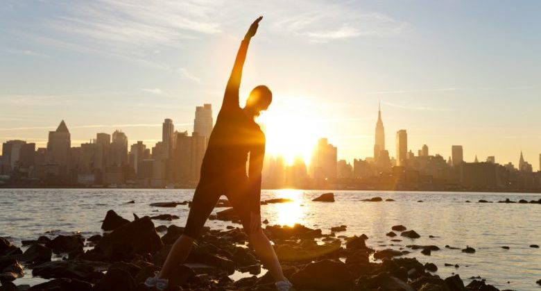 A woman runner stretching in a yoga position in front of the Manhattan skyline, New York City, United States of America, at early morning dawn sunrise