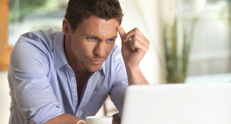 Concerned man looking at a laptop with hand on head